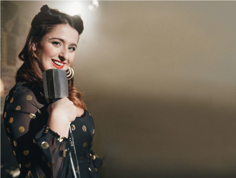 Michela Giraud sorridendo con un microfono, vestita in abito a pois per uno spettacolo di stand-up comedy